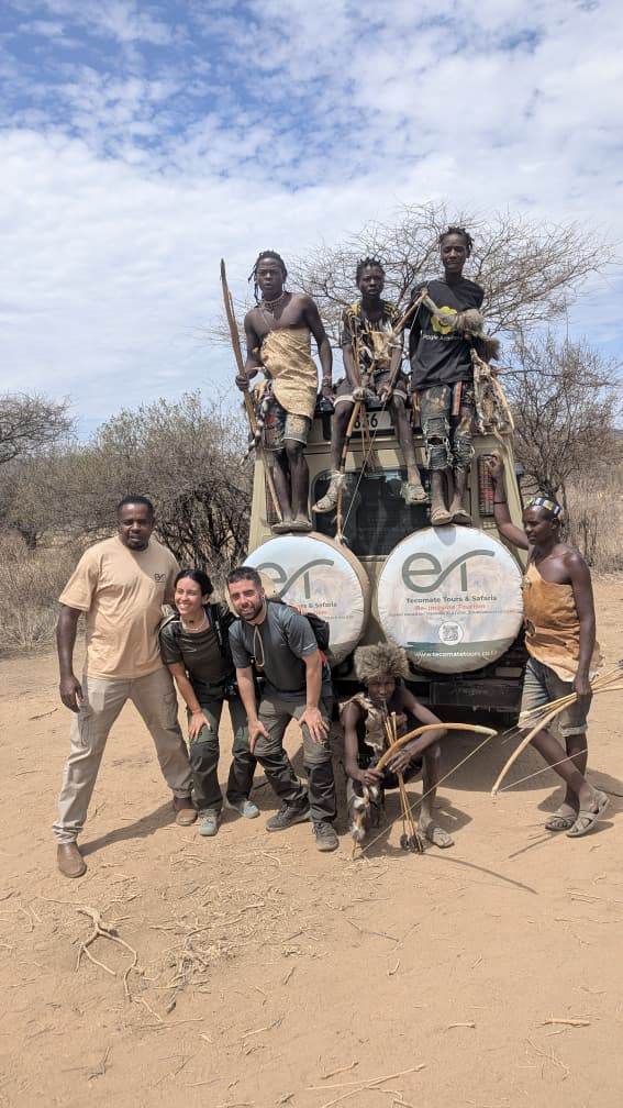 The Tecomate team and guests with a Hadzabe community group beside a branded safari vehicle