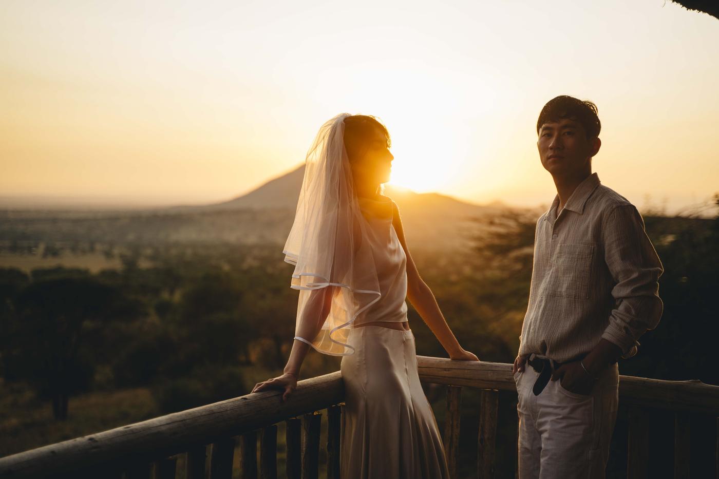 A couple on a lodge deck at sunset, the plain and a distant hill behind them