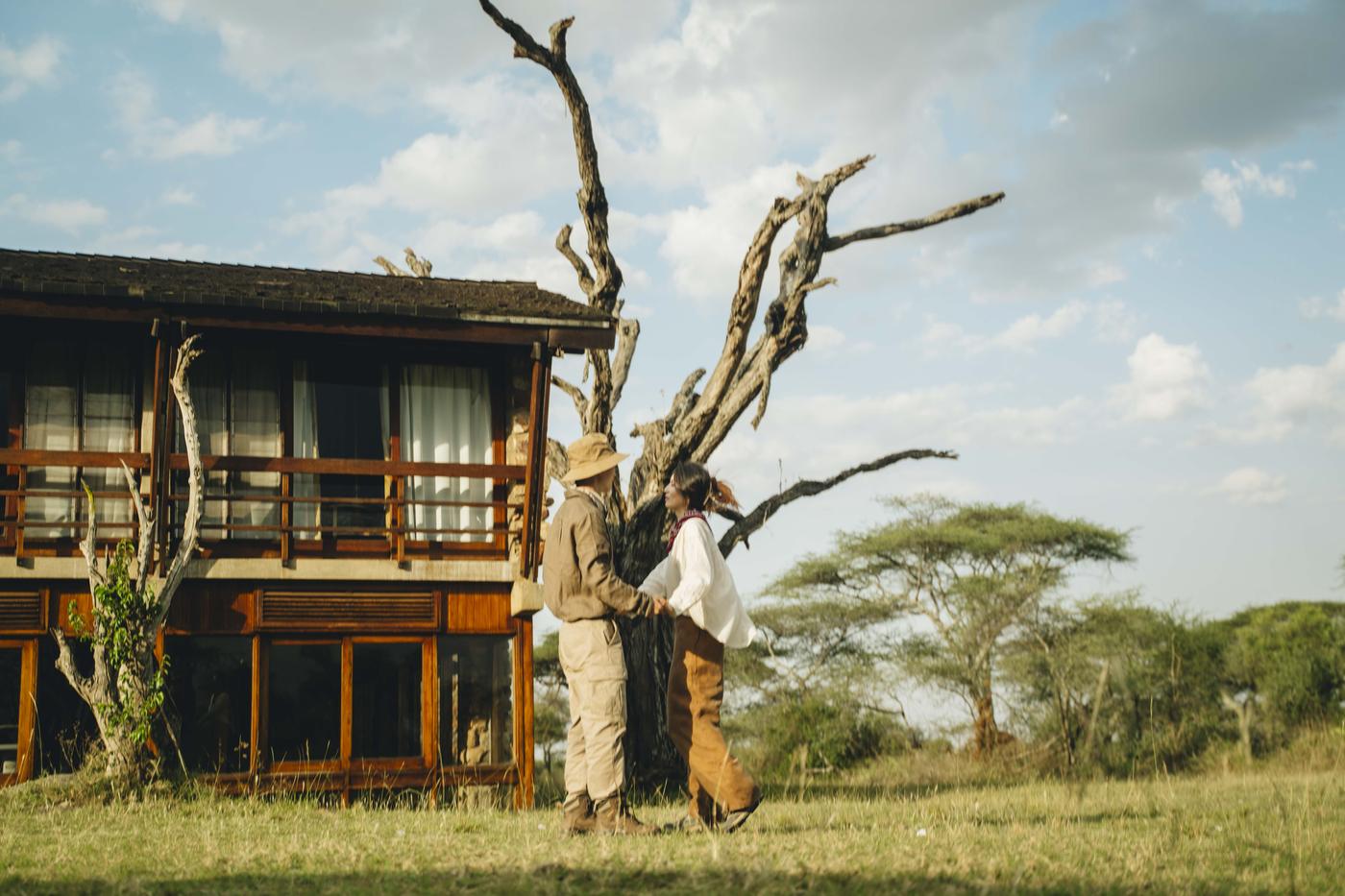Two guests walking past a timber lodge built into the trees, open bush beyond